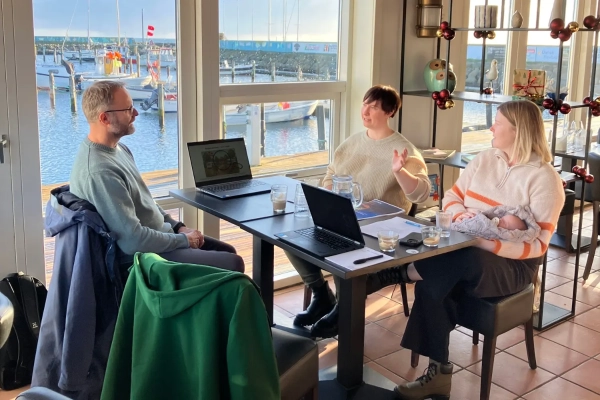 Tre personer sidder om et bord og snakker