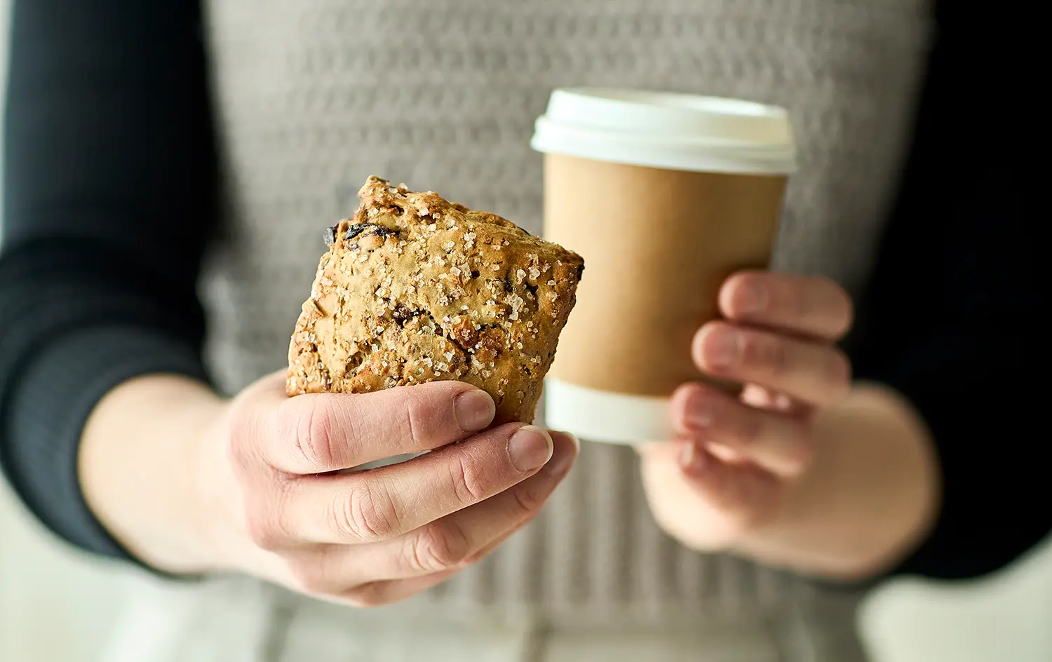 Kvinde fremviser müsliscone i den ene hånd og holder en kop kaffe i den andne.